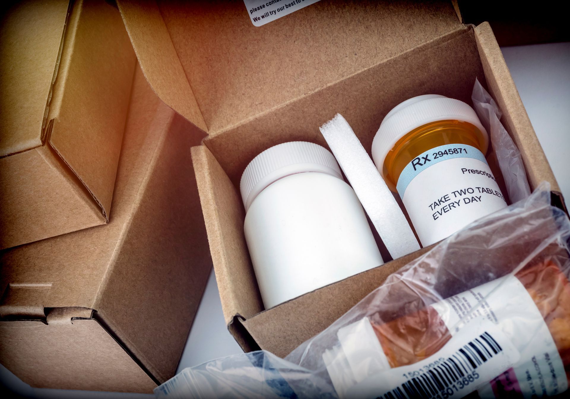 Open cardboard box with white prescription pill bottles and a clear bag inside