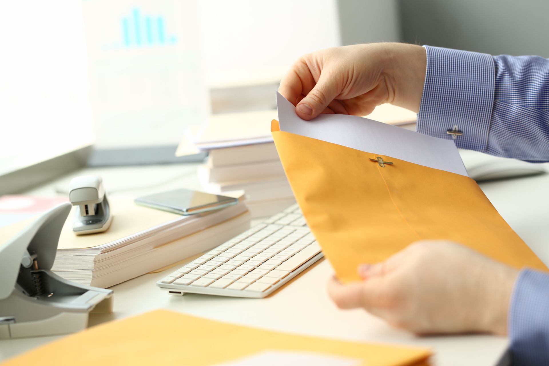 Hands opening a yellow envelope beside a keyboard and office supplies on a desk