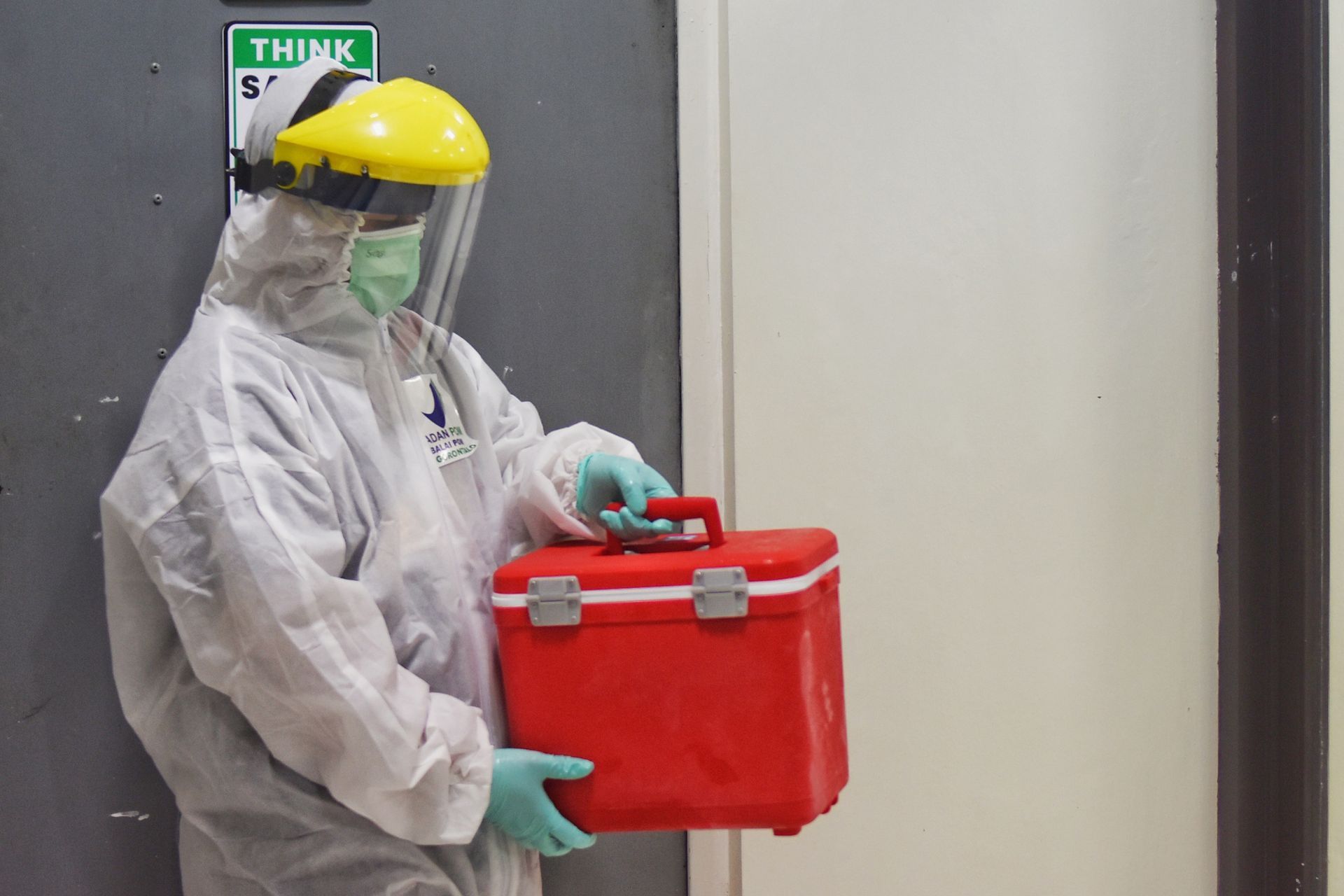 Worker in protective gear carrying a red container in a hallway