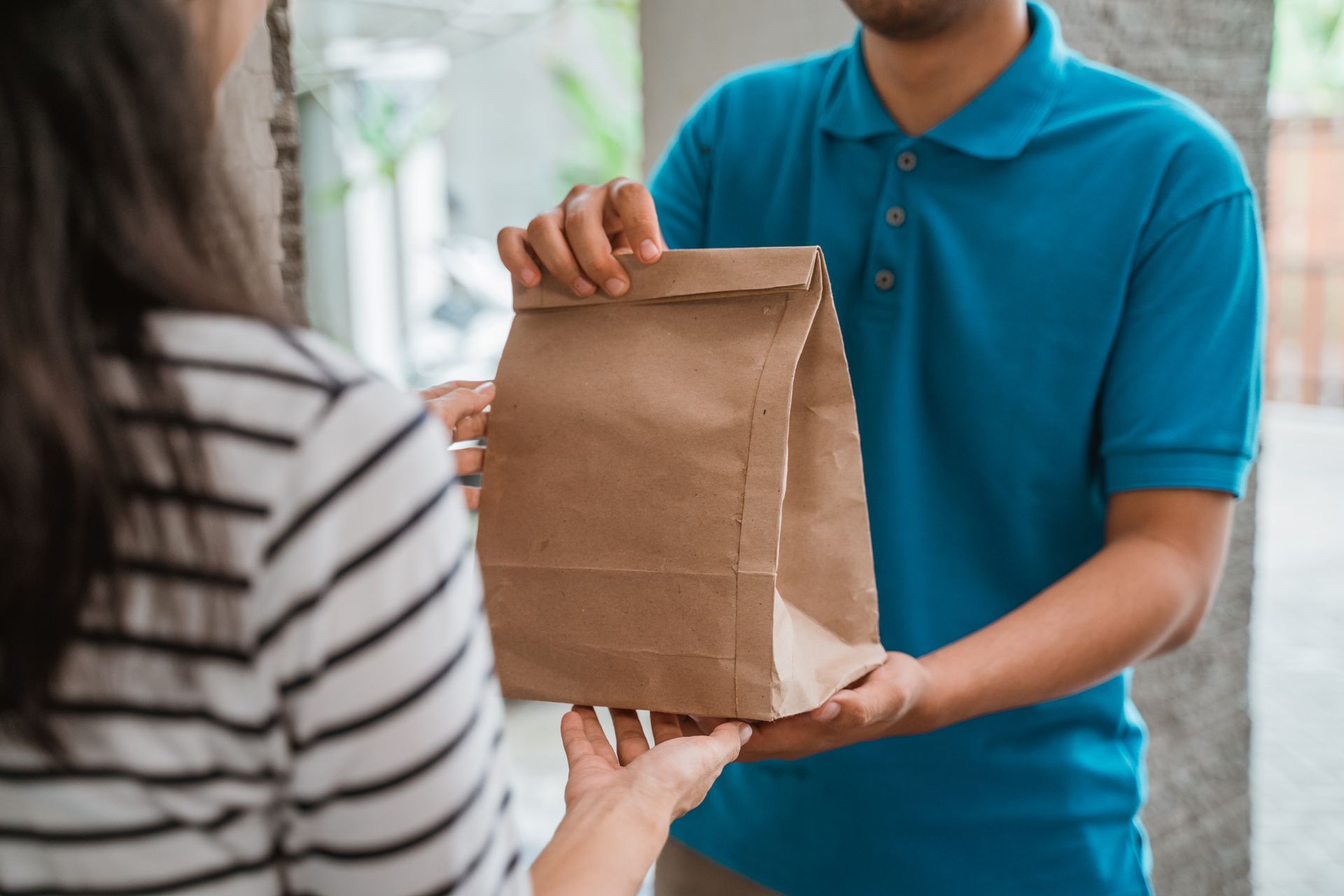 Person handing a brown paper bag to another person outdoors