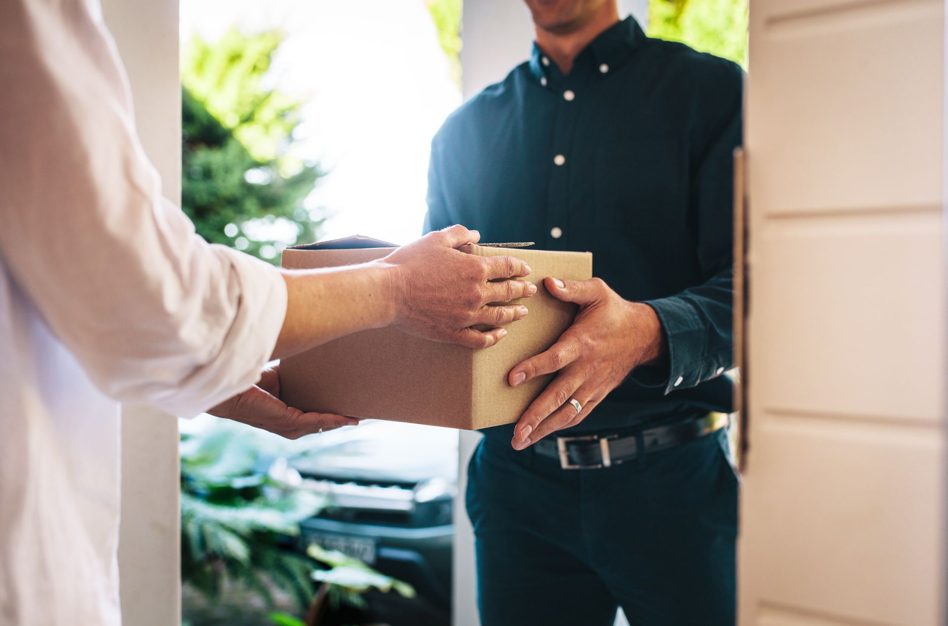 A package being handed from a delivery person to someone at a front door.