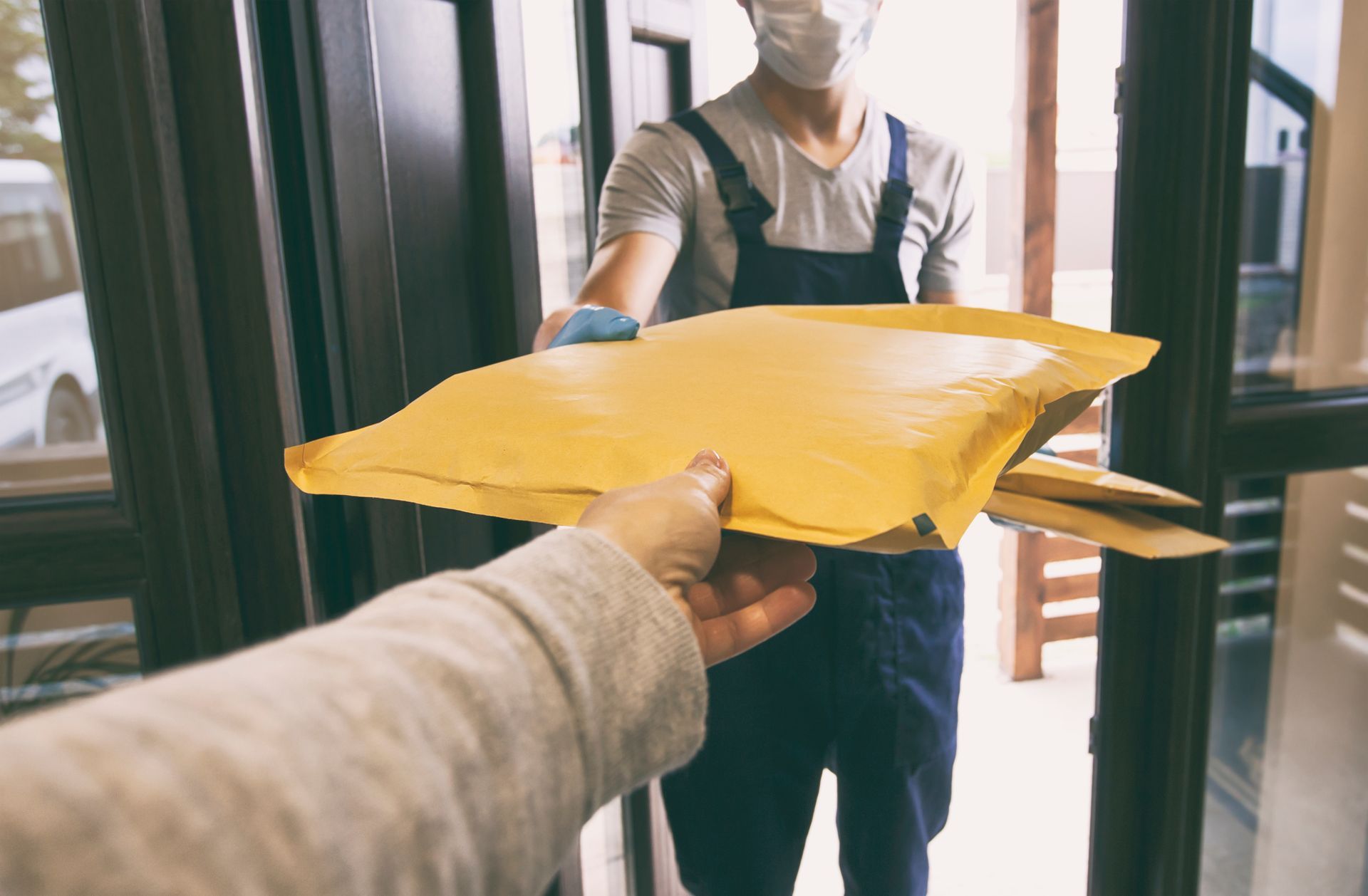 Person handing a yellow package to a masked delivery worker at the doorway