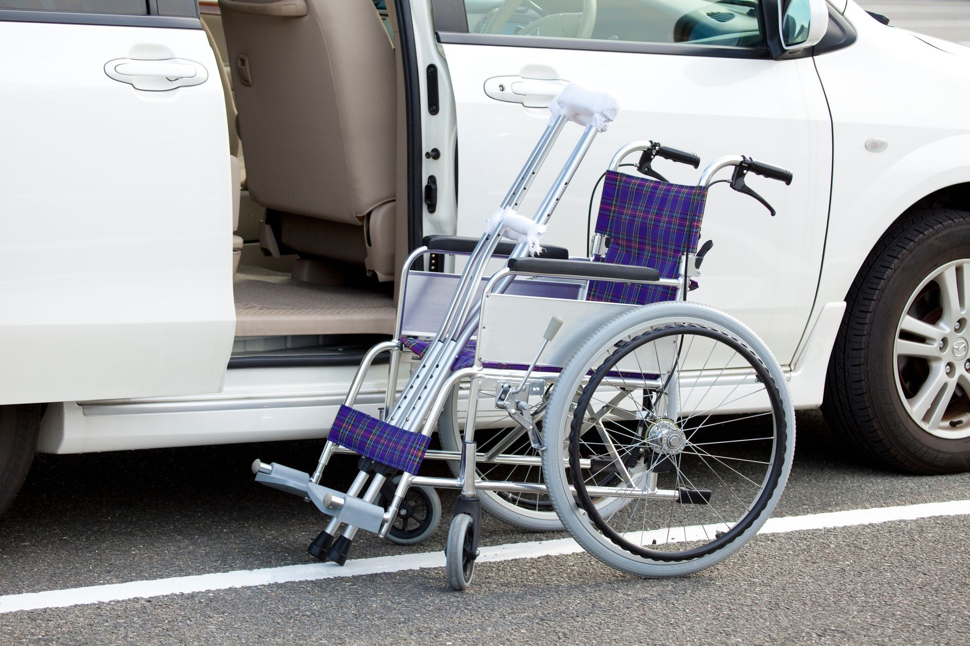 Purple wheelchair beside open car door on a sidewalk, with a white car in the background
