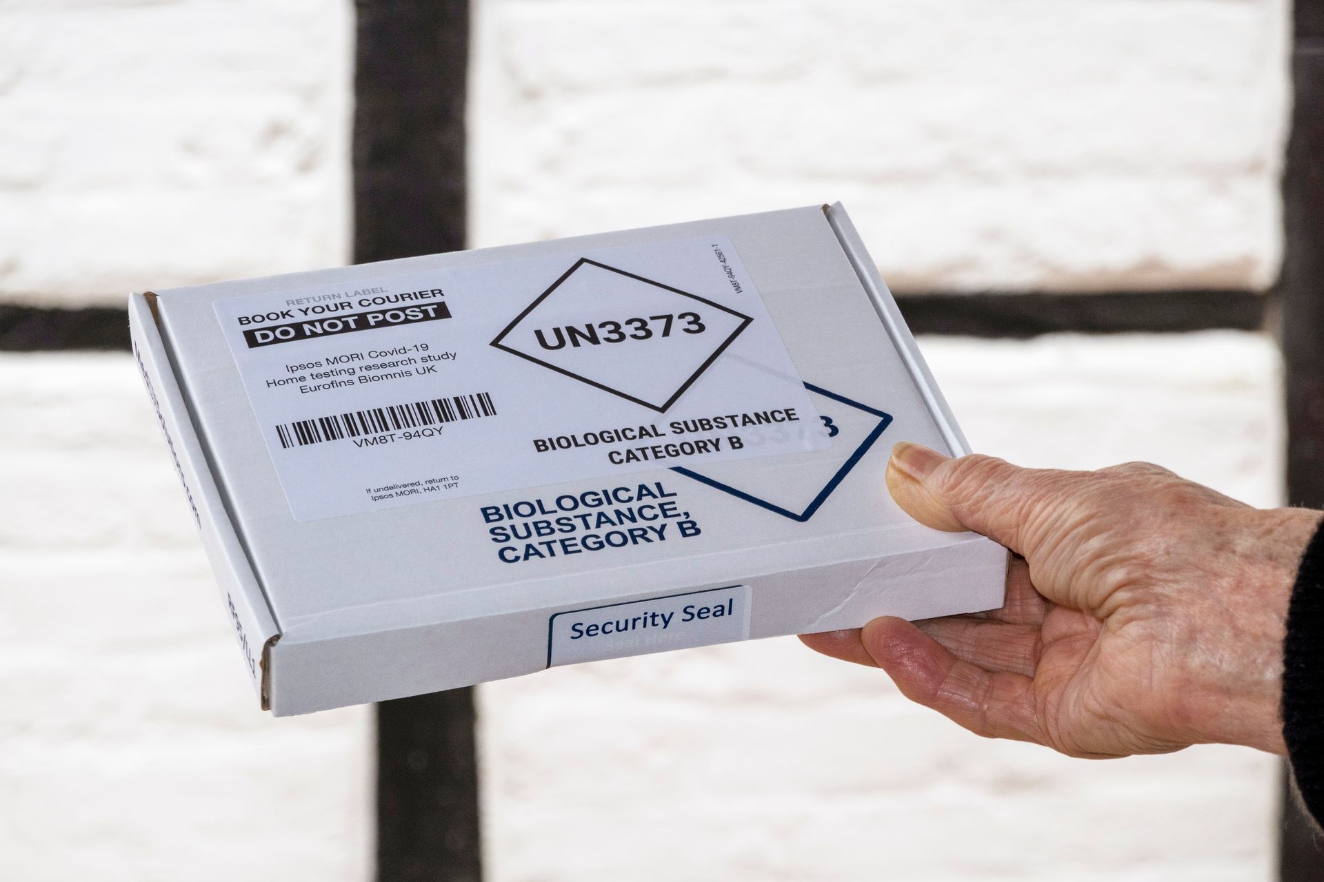 Hand holding a white shipping box with black hazard labels against a blurred background