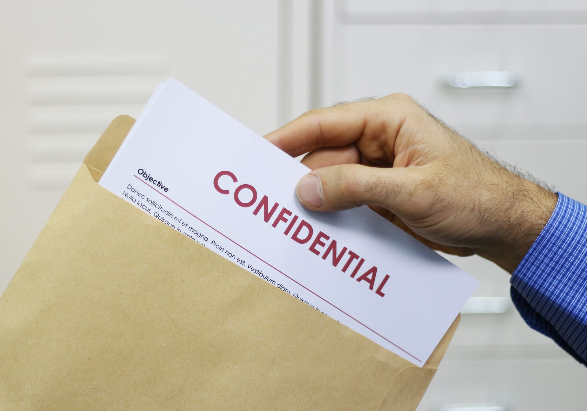 Hand placing a white CONFIDENTIAL document into a manila envelope