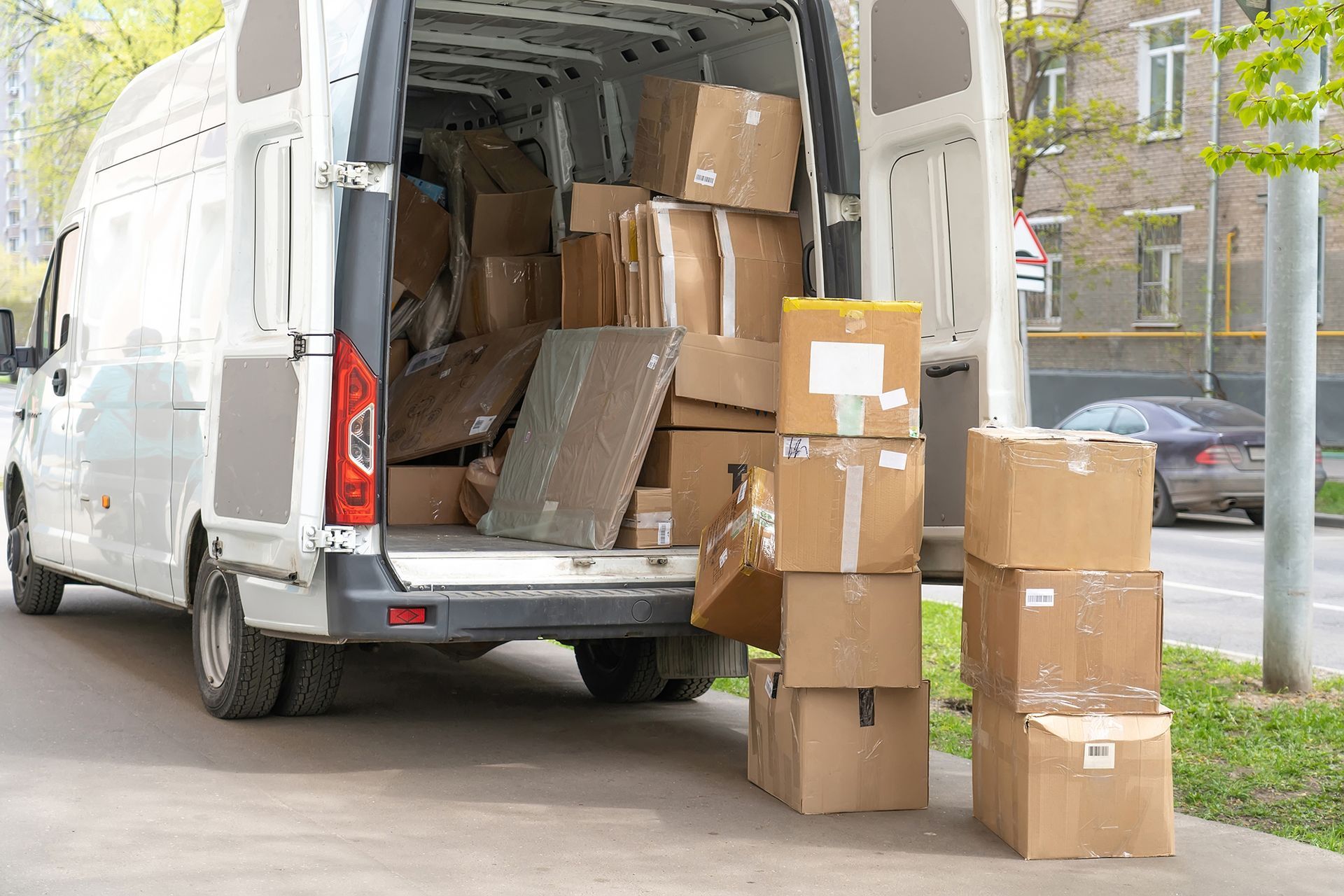 Open delivery van with stacked cardboard boxes being unloaded onto a city sidewalk