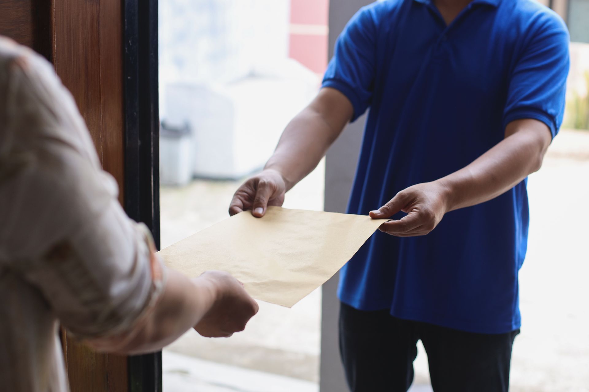 Person in blue shirt handing a cardboard box to someone at a doorway