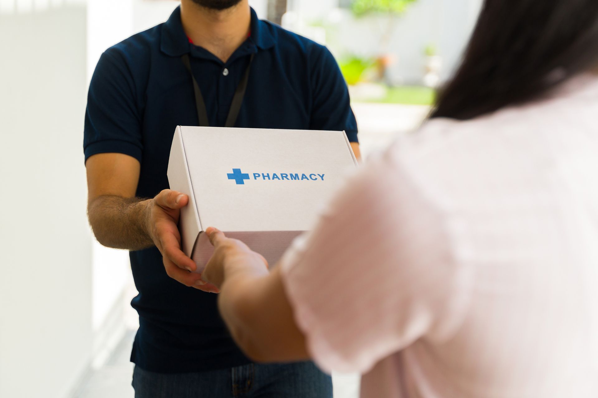 Person handing a white medical box to another person in a bright clinic hallway