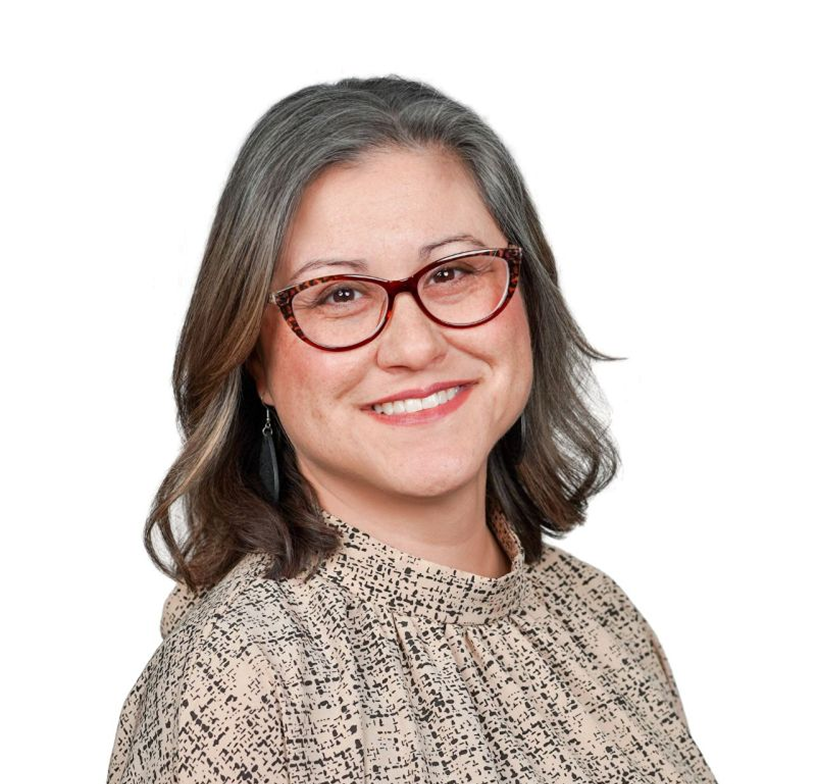 Smiling person with gray hair and glasses, wearing a patterned blouse on a white background