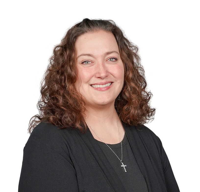 Smiling person with curly brown hair wearing a black top and silver cross necklace on a white background