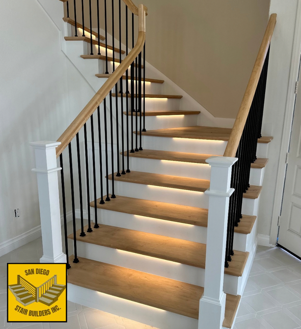 Traditional light stained maple treads and handrailing with white painted dressed posts with hats and wraps and satin black plain bar iron balusters