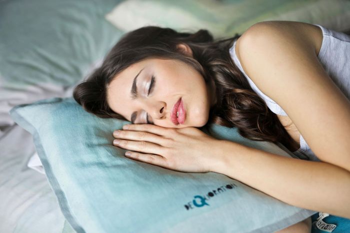 Woman sleeping on a blue pillow, face relaxed, on a bed.