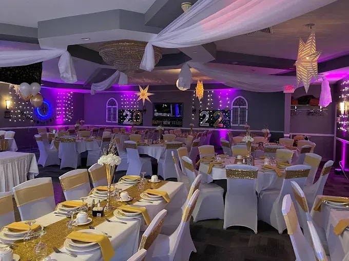 Decorated banquet hall with round tables set for a formal event, featuring white and gold accents and purple lighting.