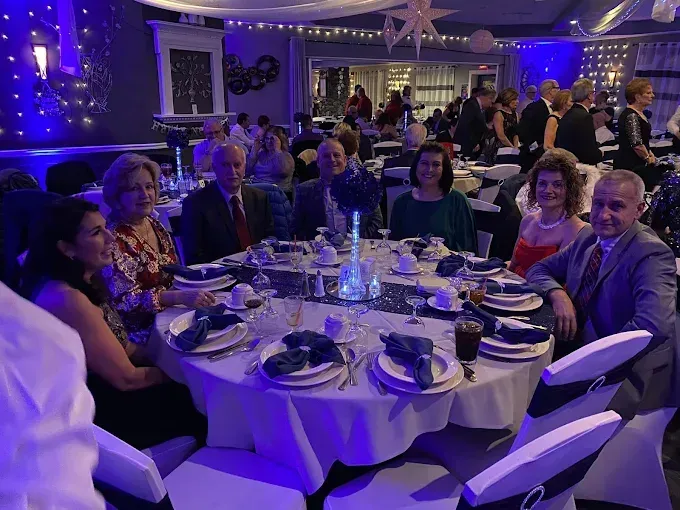 People seated around a decorated table at a formal event, lit with blue lighting.