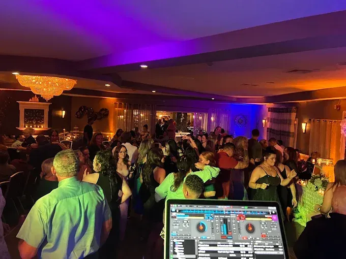 People dancing at a party with a DJ. Colorful lights illuminate the room.
