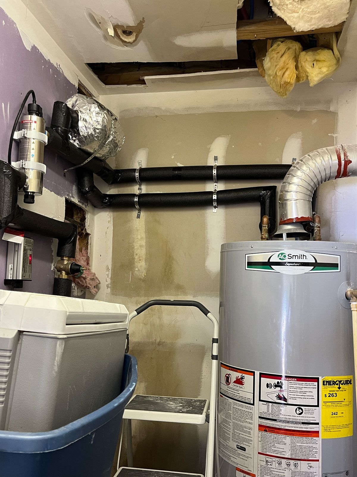 A room with a water heater and a ladder in it.