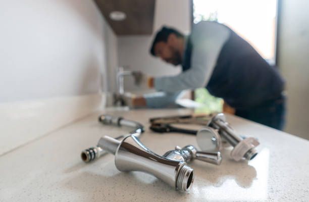 Chrome faucet fittings on a sink while a blurred person works in the background