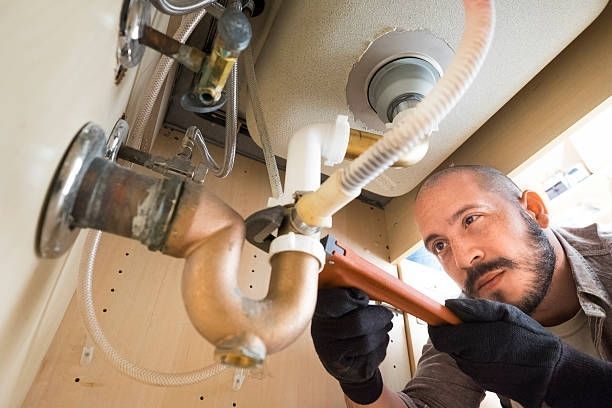 Plumber repairing pipes under a sink with a wrench in a kitchen cabinet
