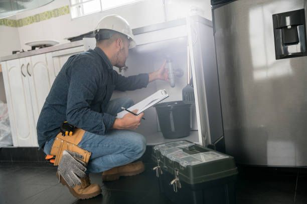 Technician kneeling beside a stainless-steel appliance, inspecting smoke with a clipboard and tool belt.