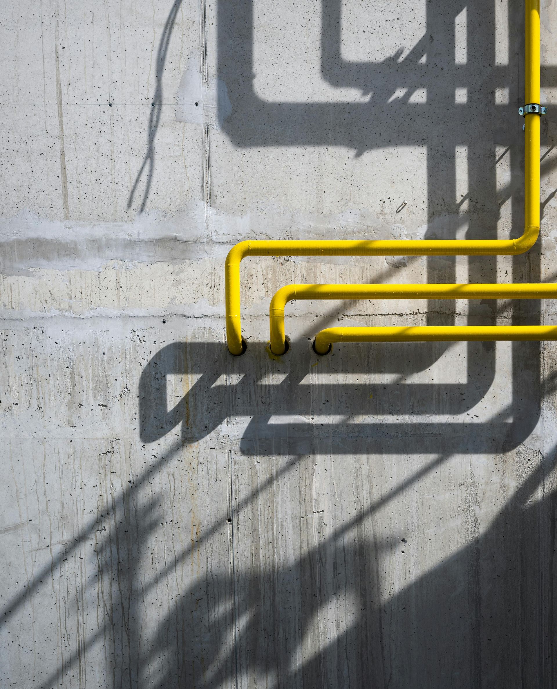 Yellow pipes casting shadows on a gray concrete wall.
