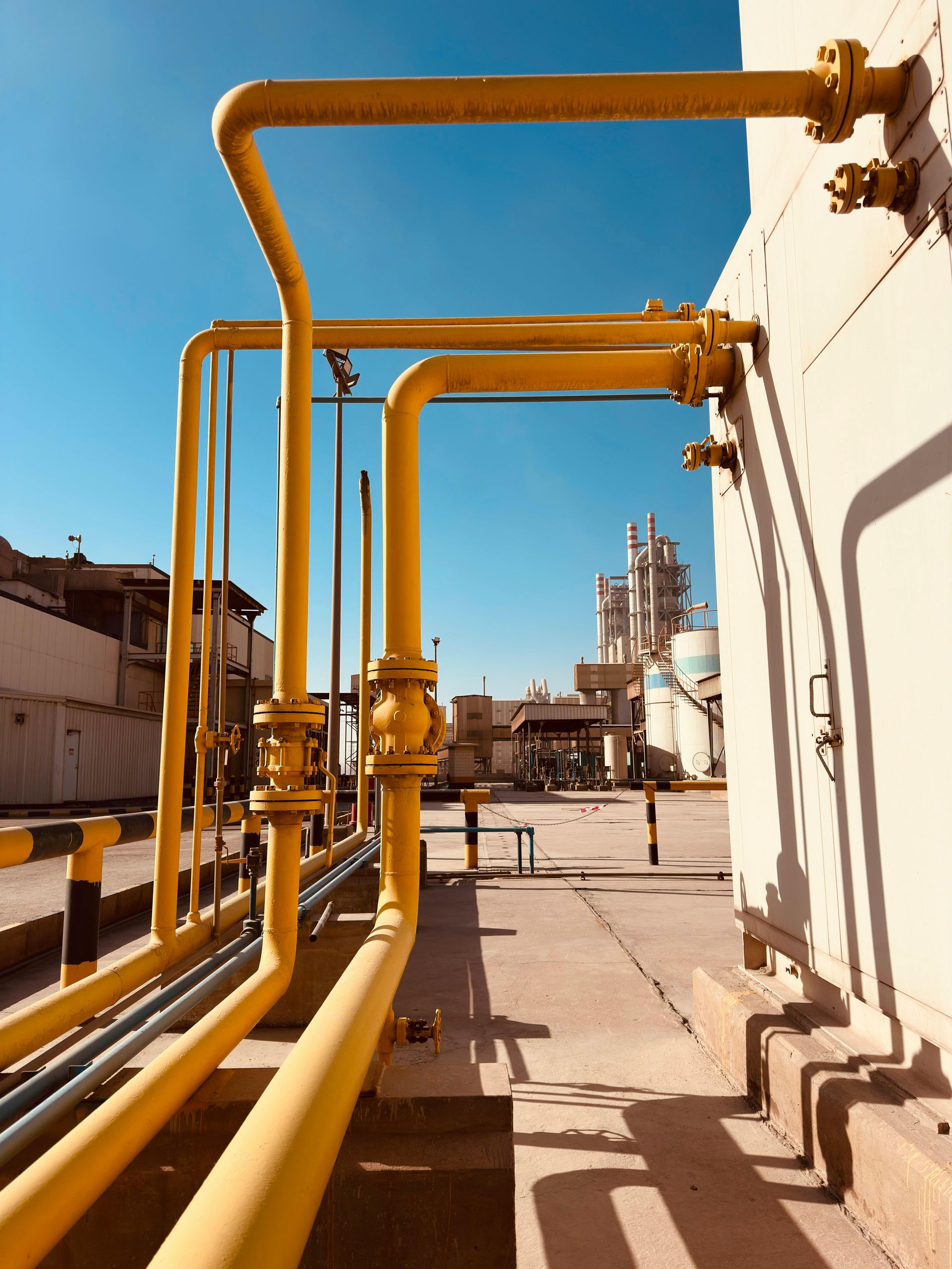 Yellow industrial pipes along a plant walkway under a blue sky