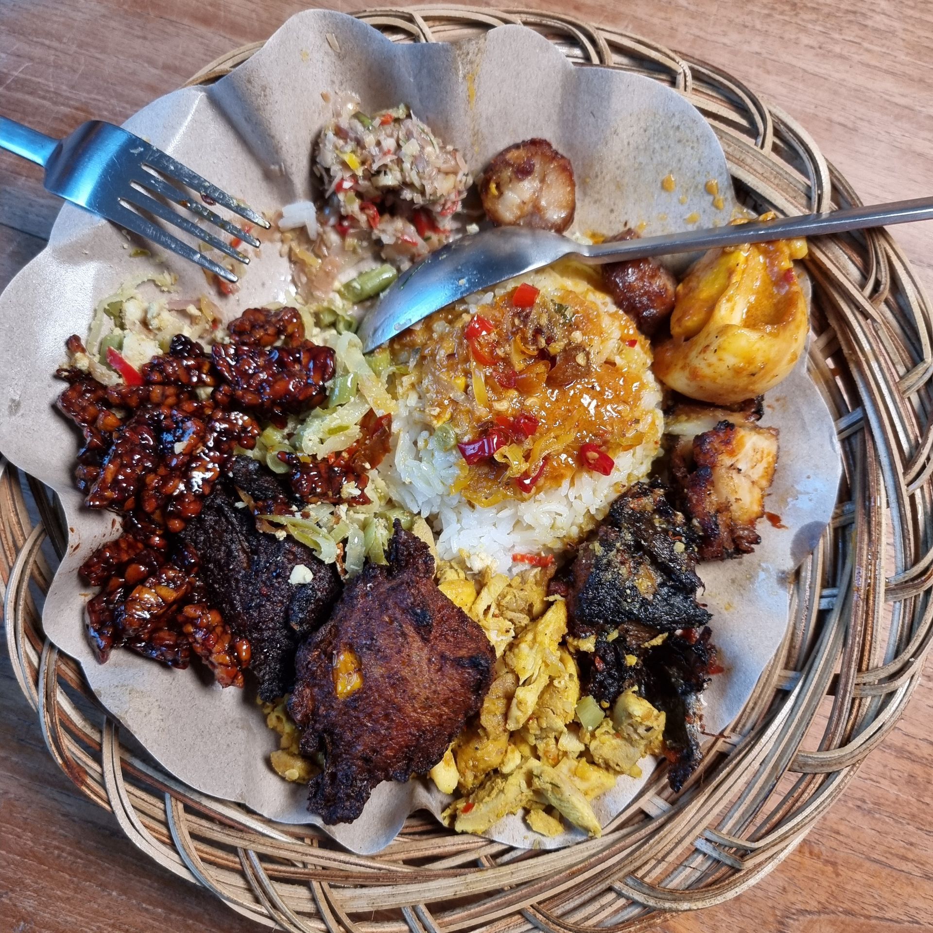 Een bord Indonesisch eten: rijst, vlees, groenten en kruiden, gerangschikt op een gevlochten schaal.