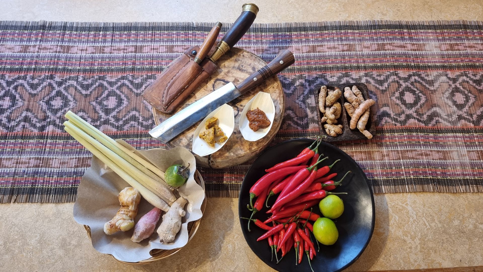 Bovenaanzicht van Indonesische kookingrediënten: chilipepers, kruiden, limoen, specerijen en messen op een houten snijplank.