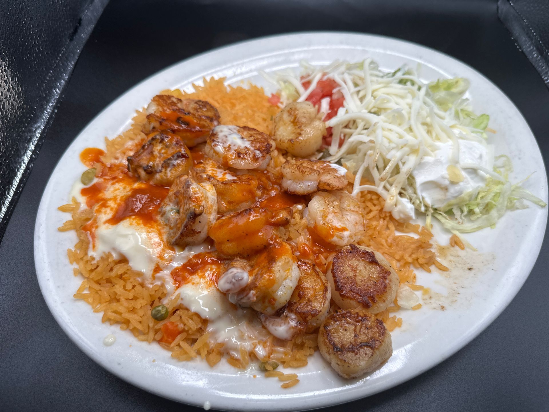 Plate of Mexican food: shrimp in sauce over rice, with sides of lettuce, sour cream, and tomatoes.