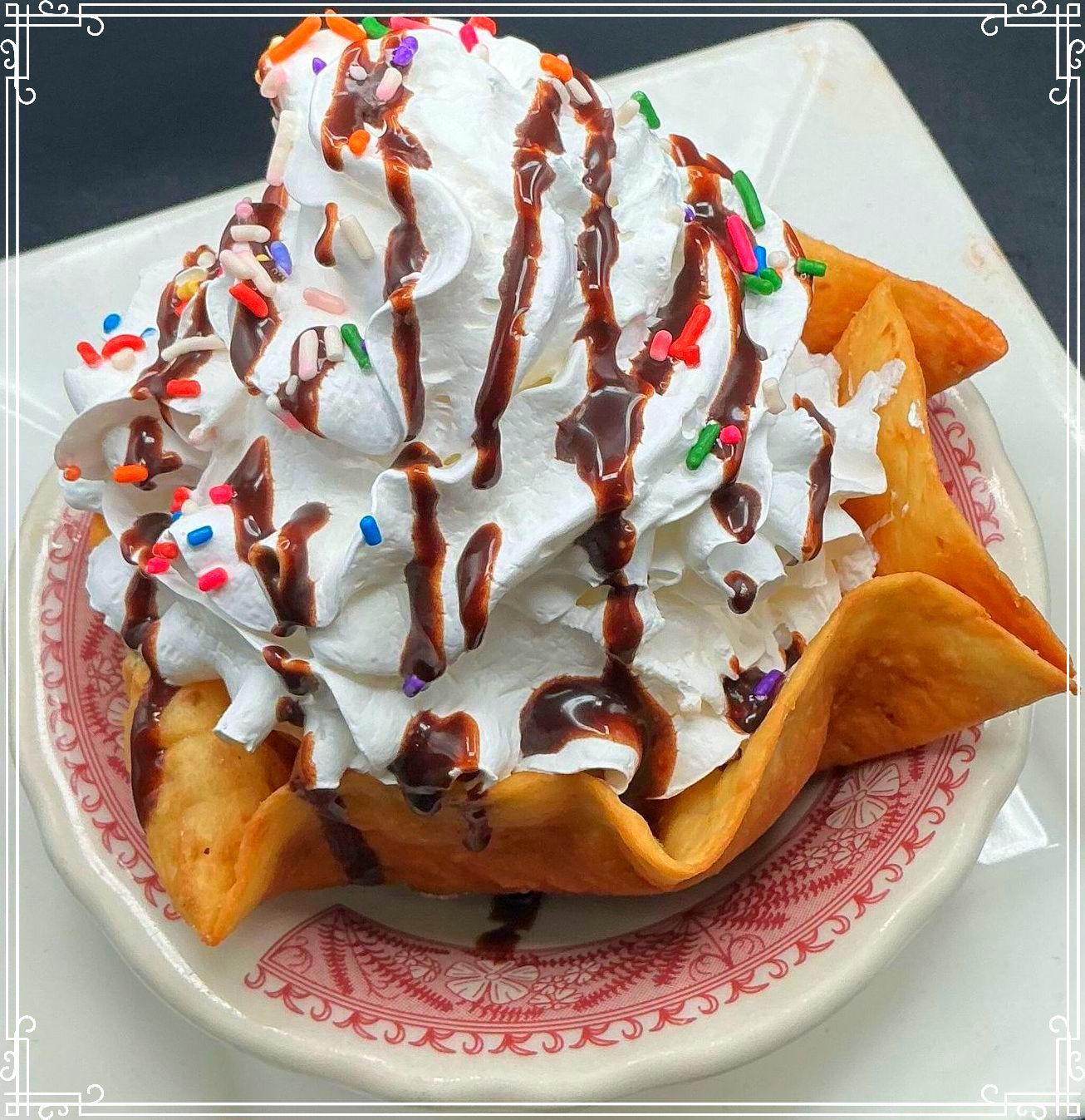 Fried pastry bowl filled with whipped cream, chocolate syrup, and sprinkles.