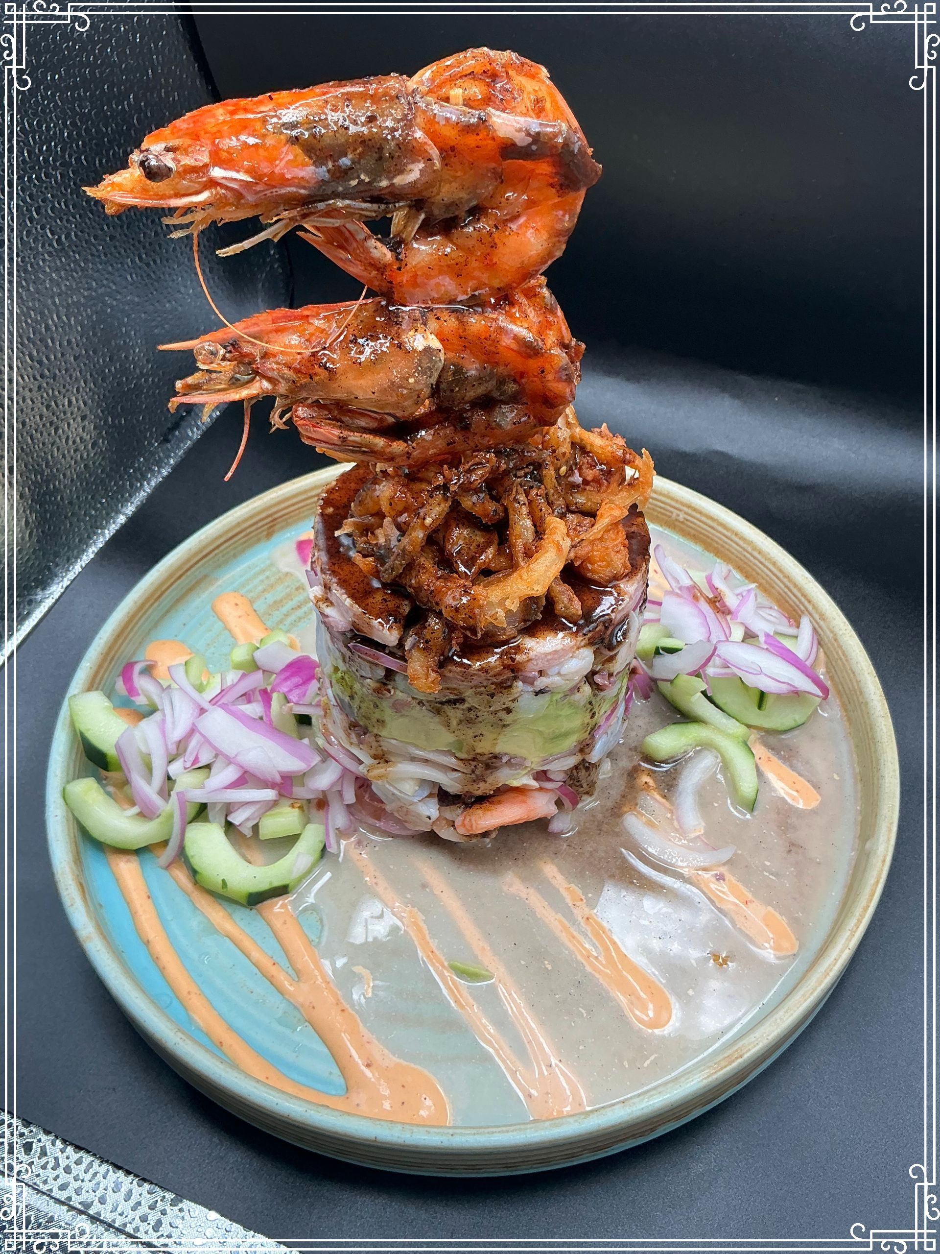 Tower of seafood, stacked on a plate with sauce, shrimp on top, avocado and onion layers.