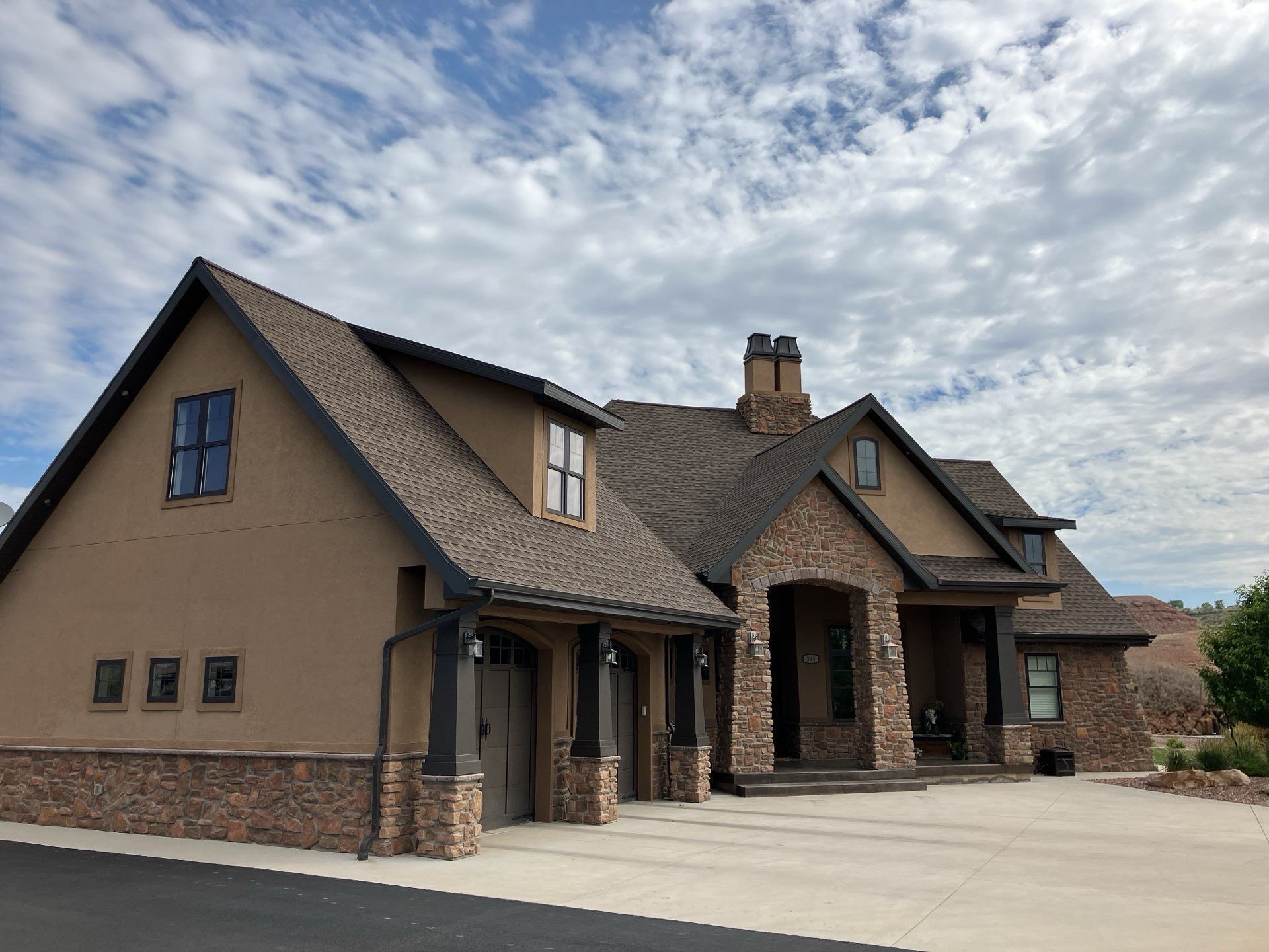 Brown stucco house with stone accents, dark roof, cloudy sky.