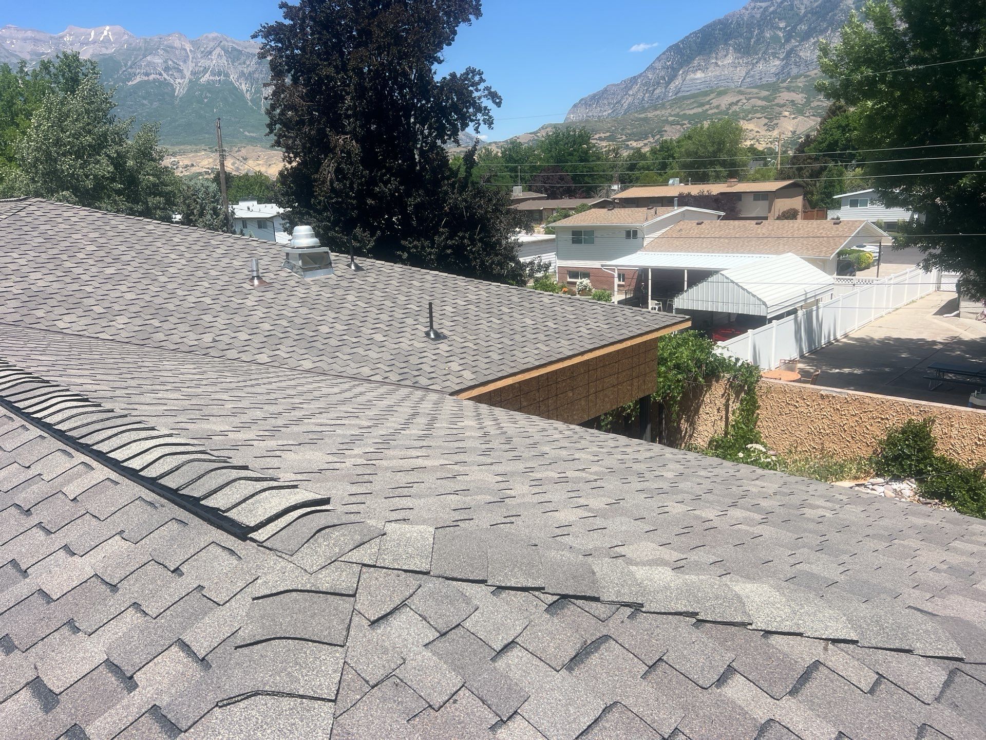 Gray shingle roof of a house with mountains in the background, under a bright, sunny sky.