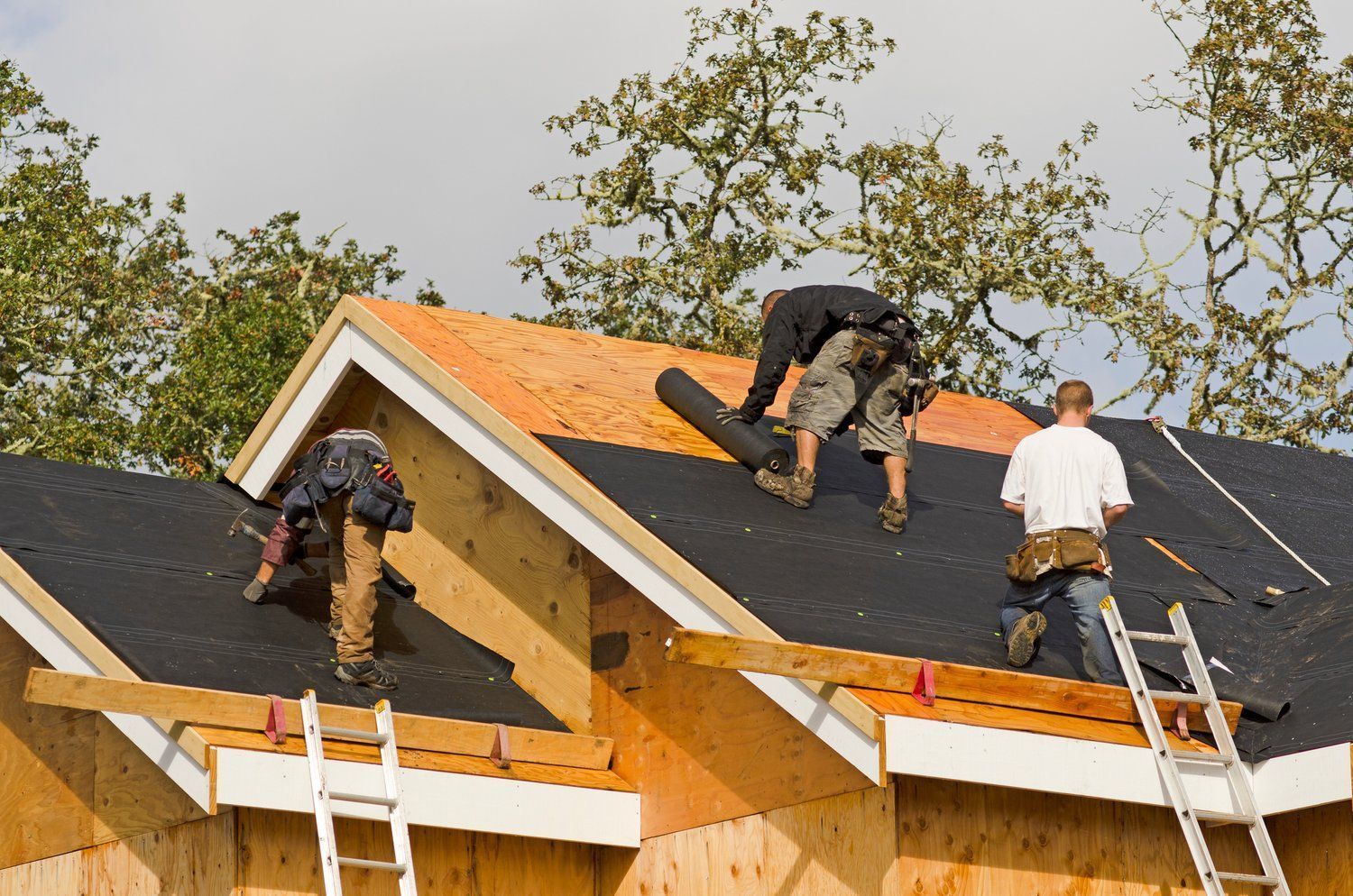 Construction workers installing roofing on a wooden house frame outdoors.