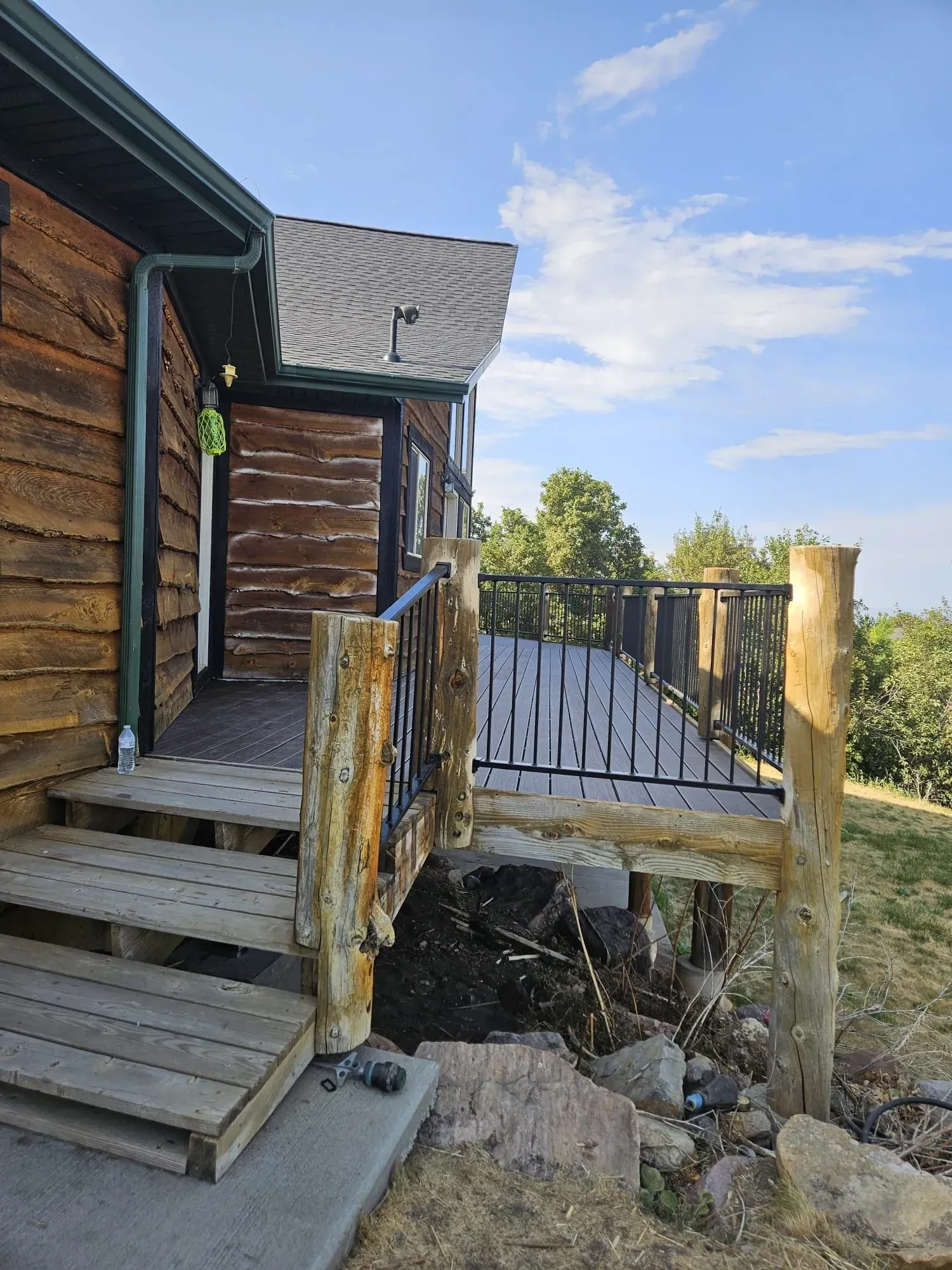 Wooden deck and steps leading to a house with a black railing, set against a blue sky.
