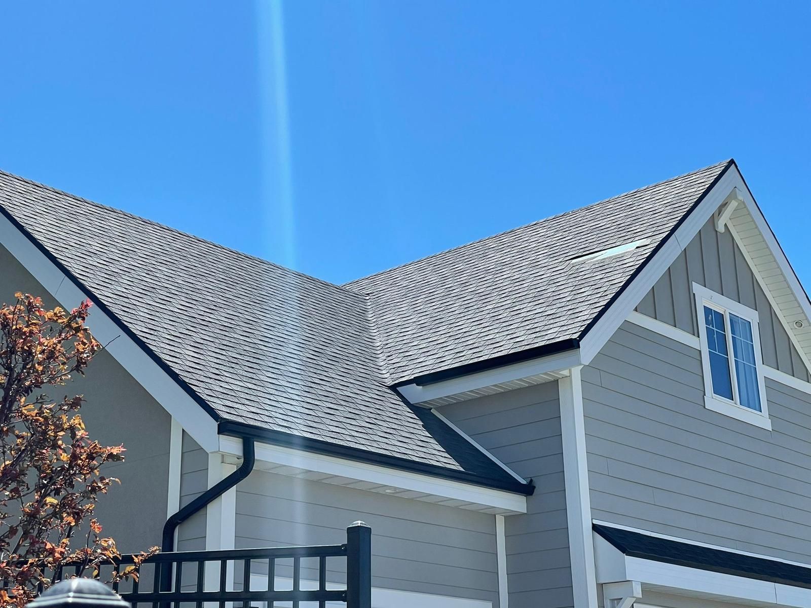 Two dormer windows with wood frames on a slate roof under a blue sky.