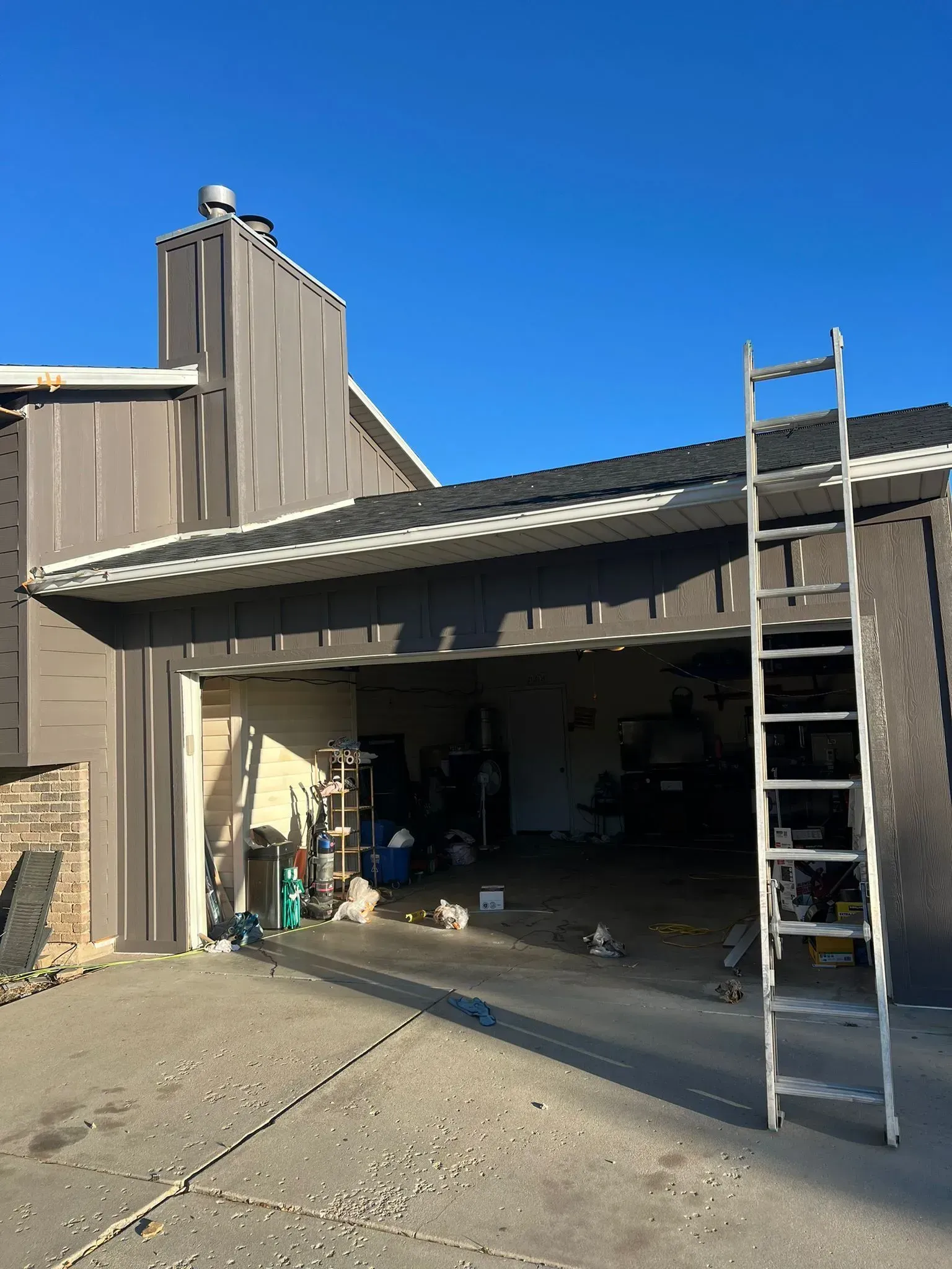 A large, tan and stone house with a brown roof and garage doors on a sunny day.