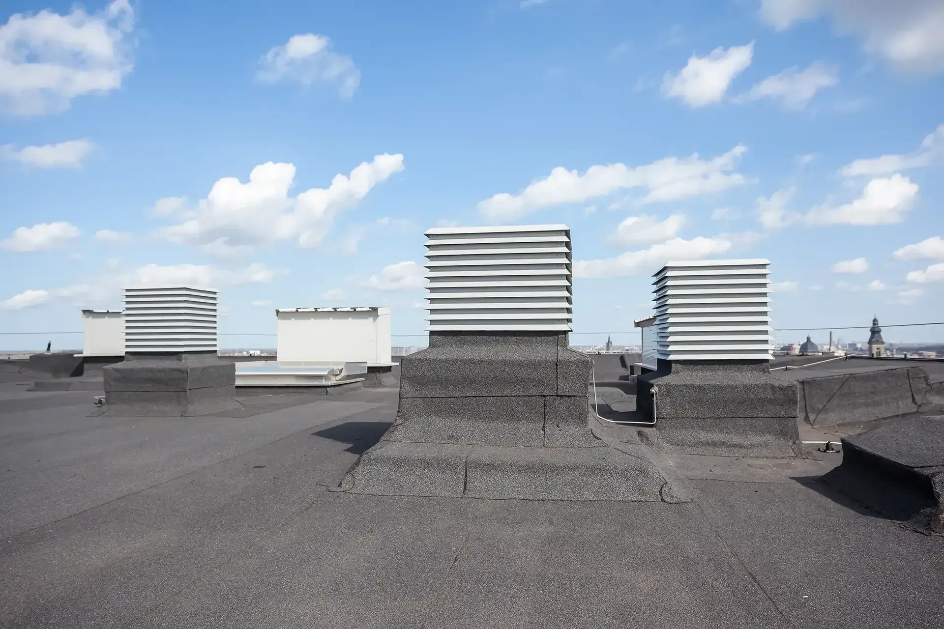 Rooftop with several rectangular vents against a partly cloudy sky.
