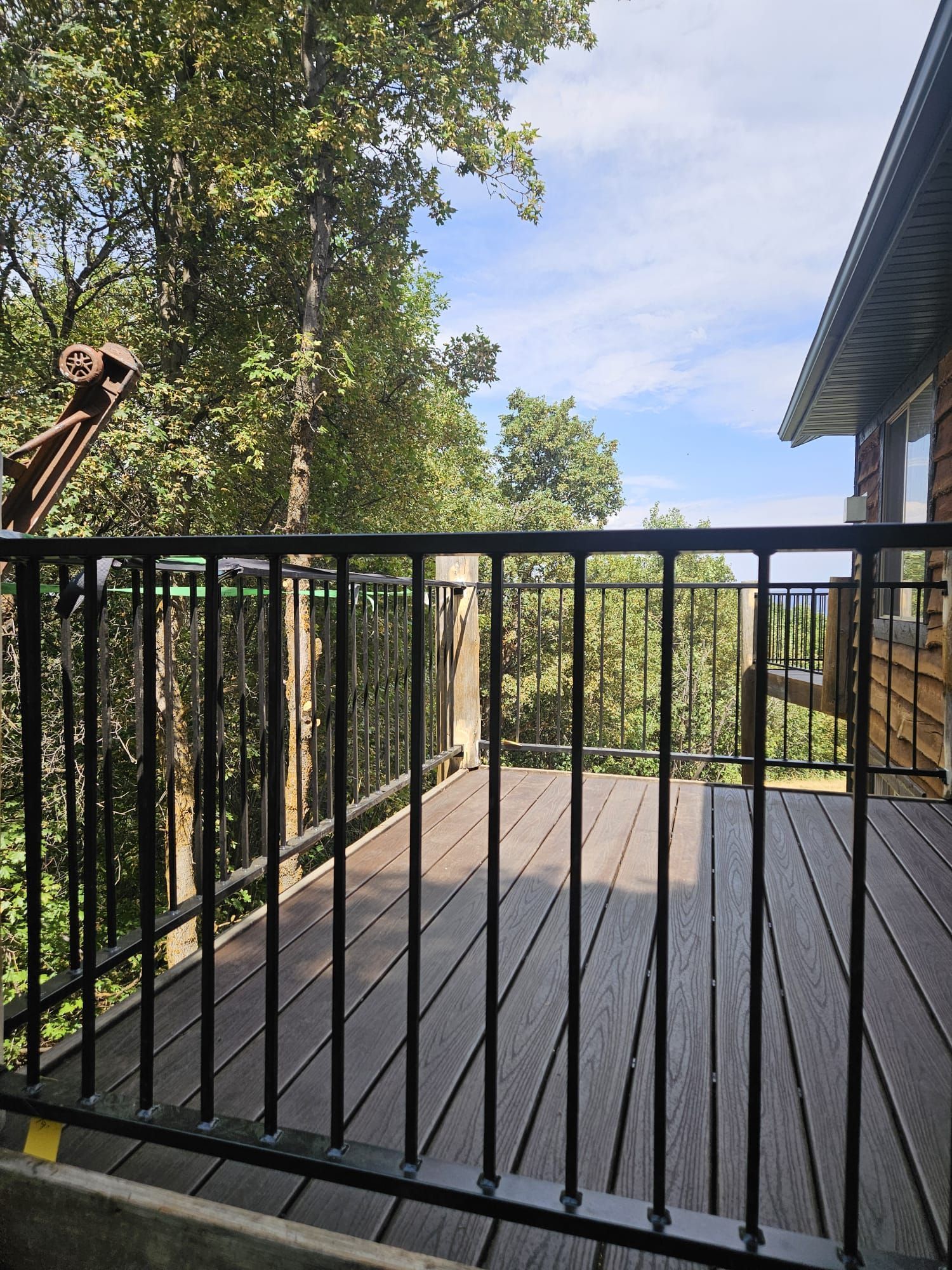 Deck with black railing overlooking trees and a blue sky. Brown deck boards.