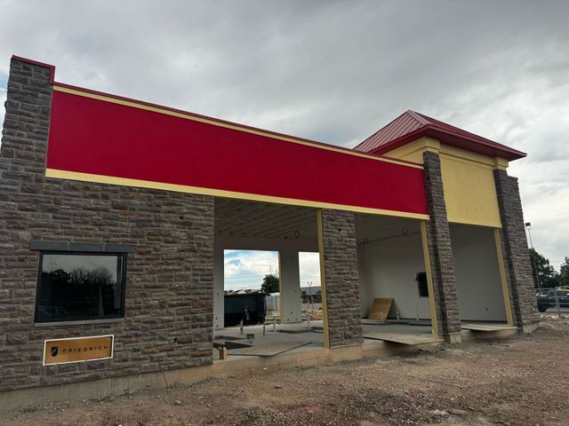 Exterior view of a car wash building under construction; red, tan, and gray brick exterior with a gray sky.