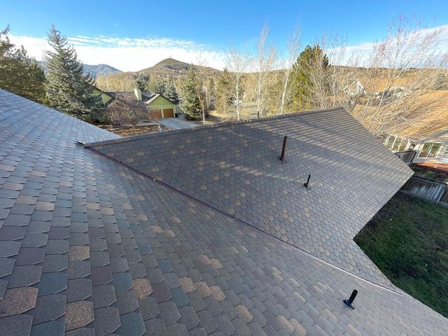 View of a shingled roof with a mountain backdrop under a blue sky.