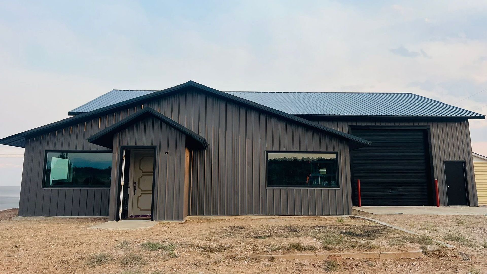 Grey wooden building with large garage door and two windows.