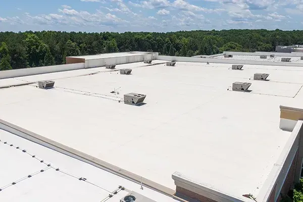 Flat, white commercial roof with several HVAC units against a backdrop of trees and a partly cloudy sky.