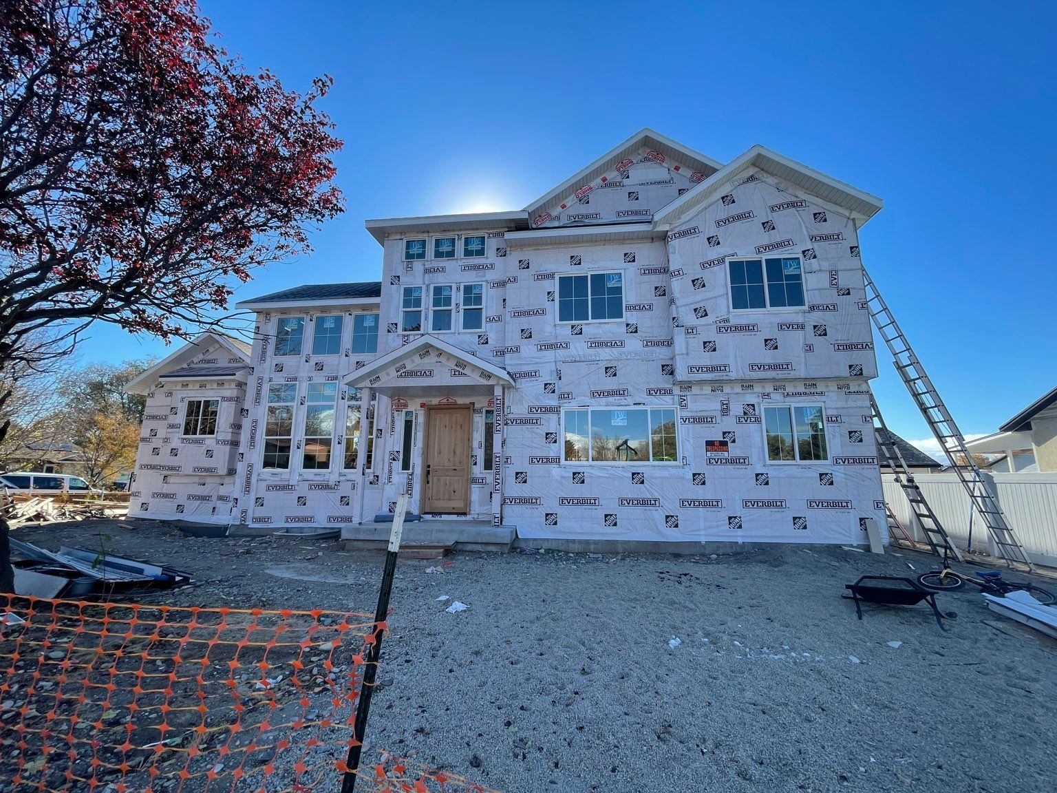 New house under construction, covered in pink weather-resistant material, with ladder and blue sky.