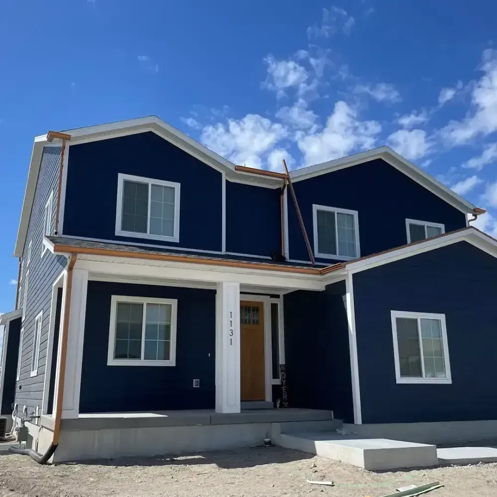 Two-story house with blue siding, white trim, and a yellow door, against a blue sky.