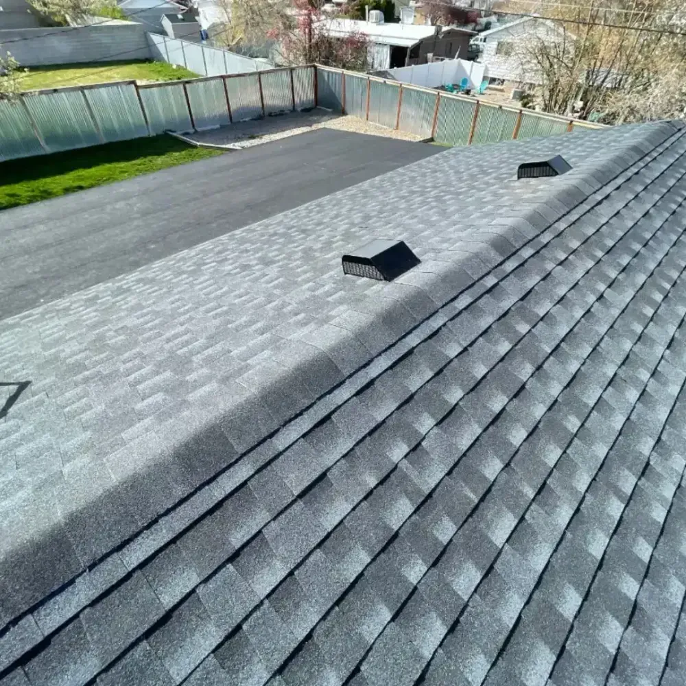 Overhead view of a gray asphalt shingle roof with two vents, a black driveway, and a green lawn.
