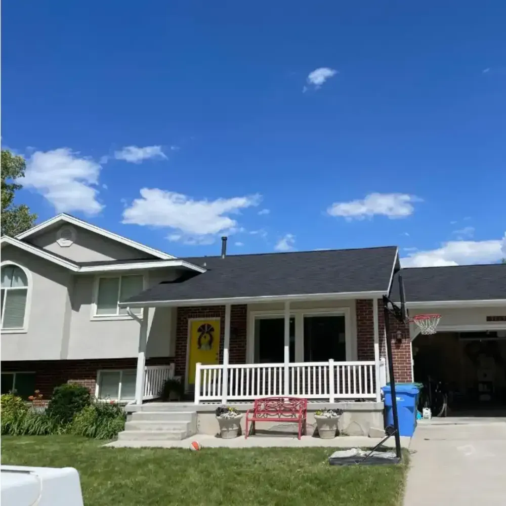 House with porch and yellow door under a bright blue sky, basketball hoop in driveway.