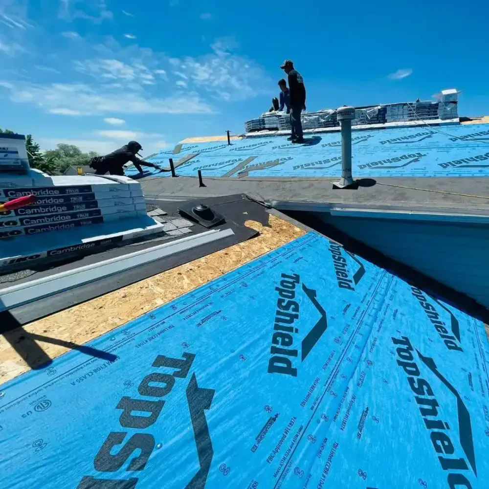 Roofers working on a building; blue underlayment and shingles. Sunny day, clear sky.