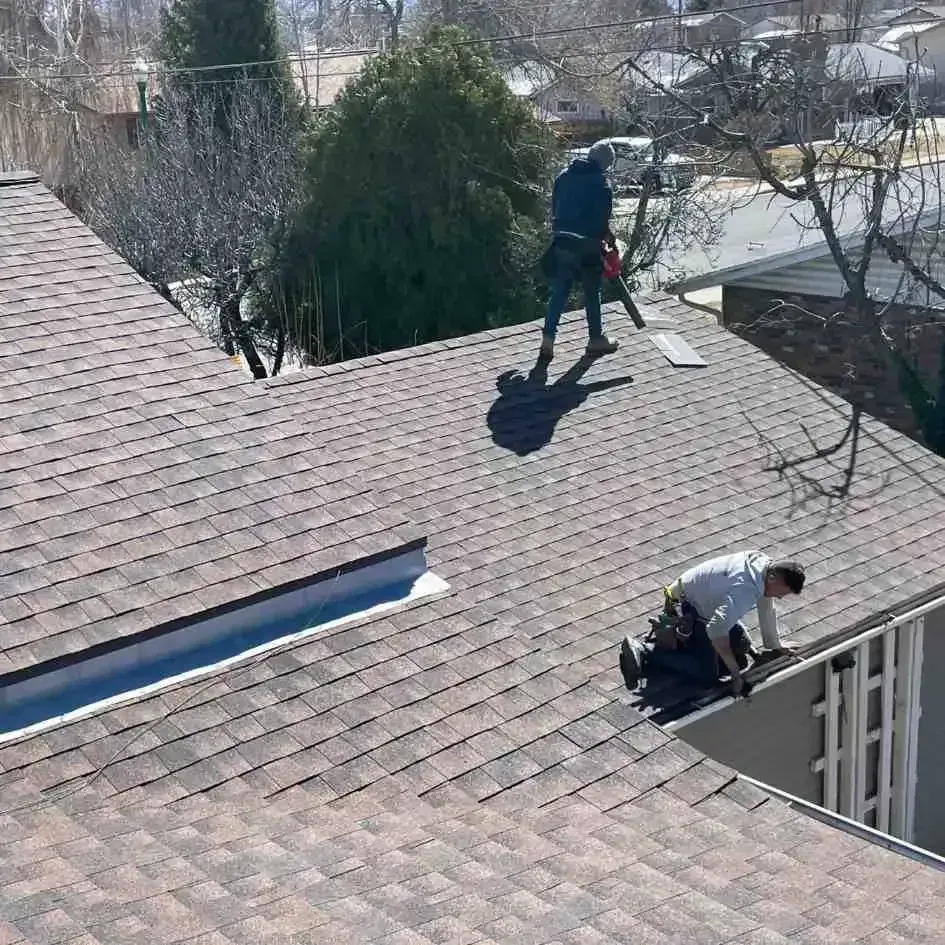 Two roofers installing shingles on a house roof on a sunny day.
