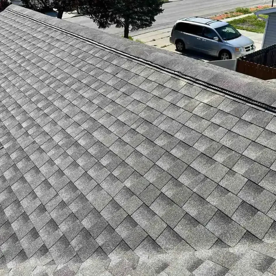 Gray asphalt shingle roof with a dark ridge line, viewed from above, with a street and vehicle in the background.