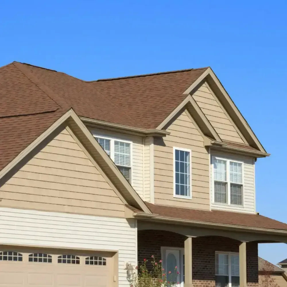 Two-story beige house with brown roof and garage, under a clear blue sky.
